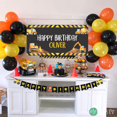 Construction themed birthday party decorations. A black banner with yellow and black stripes reads &#39;Happy Birthday&#39;. The table is decorated with a construction themed cake, cupcakes, and other treats.