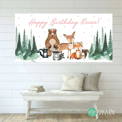 A white banner with the text &#39;Happy Birthday&#39; in pink lettering. The banner features a watercolor illustration of a brown bear, a deer, a fox, a raccoon, and a skunk. The animals are surrounded by green trees and gold glitter.