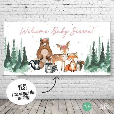 Welcome Baby banner with a pink and white color scheme. The banner features a brown bear, a deer, a fox, a raccoon, and a skunk with floral crowns. The animals are surrounded by green trees and gold glitter.