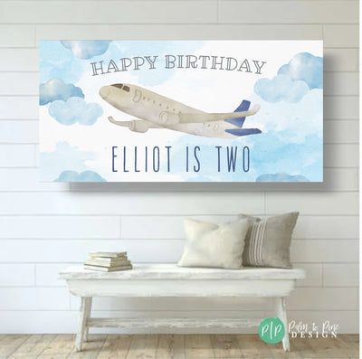 A blue and white airplane flying in a blue sky with white clouds. The text &#39;Happy Birthday&#39; is at the top of the banner. The text &#39;Elliot is Two&#39; is at the bottom of the banner.