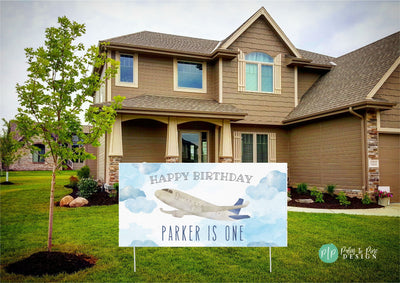 A blue and white birthday sign with an airplane flying through clouds. The sign reads &#39;Happy Birthday Parker is One&#39;