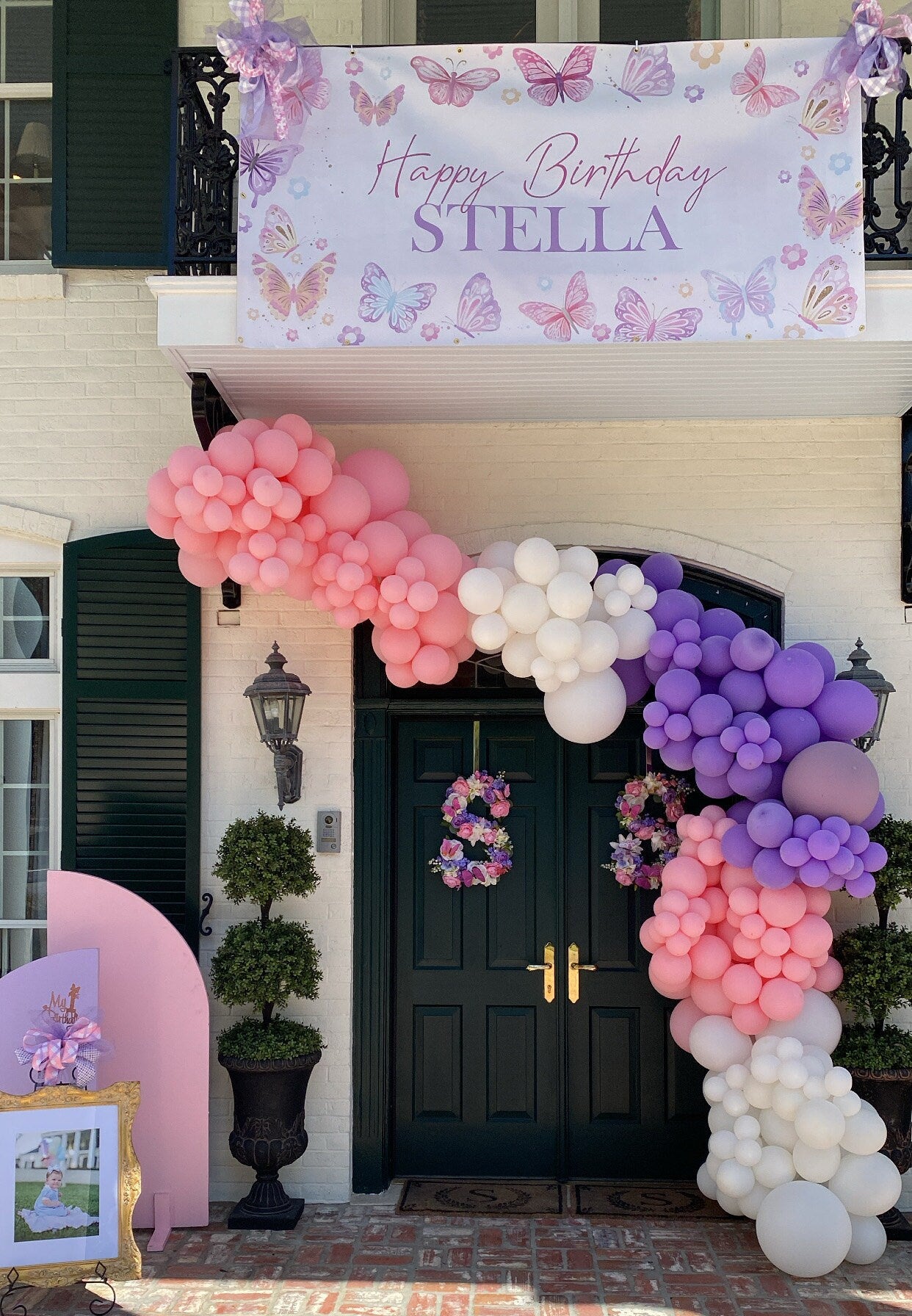 girls butterfly birthday party entrance with welcome banner and pink, purple and white balloon garland