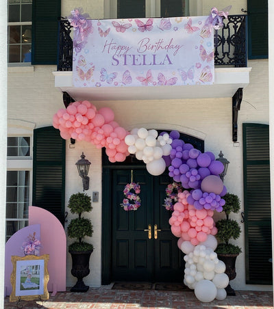 butterfly birthday banner with watercolor pastel butterflies and balloon garland at entrance of house