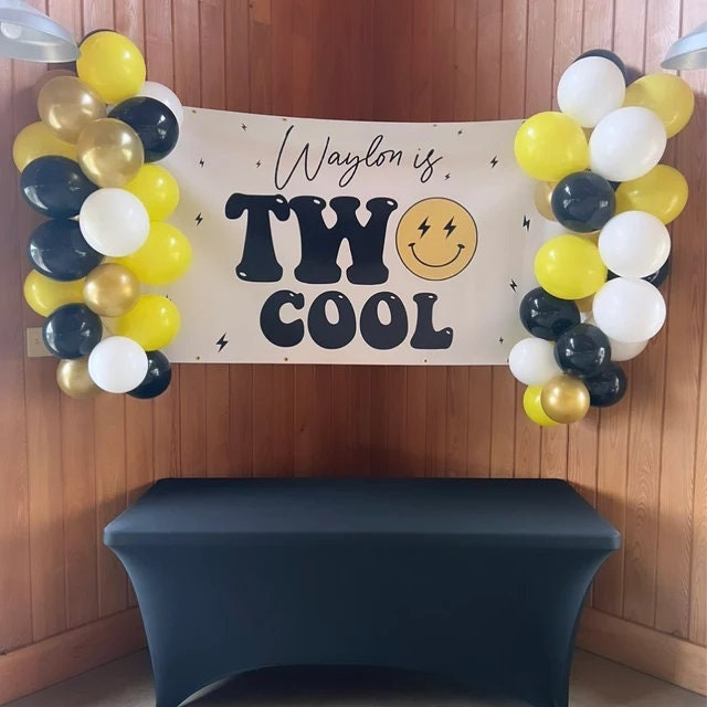 &quot;Modern &#39;Two Cool&#39; birthday party banner decorated with a smiley face and lightning bolts in a sleek, contemporary style for a second birthday celebration with yellow, gold and white balloon garland