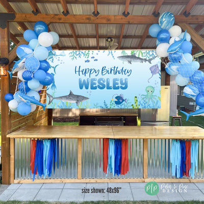 Personalized Shark Birthday Banner with Watercolor Sealife Animals surrounded by blue balloon garlands with inflatable sharks and fishing nets