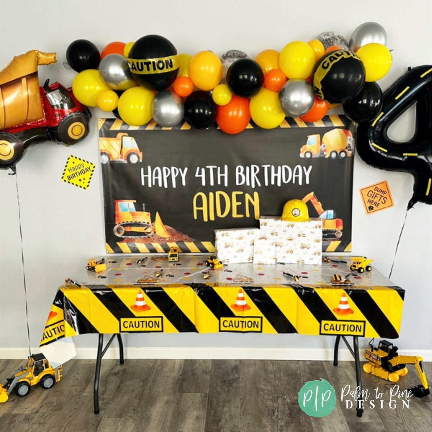 A construction themed birthday party set up with a personalized black and yellow banner and balloon garland with caution signs and construction equipment decorations